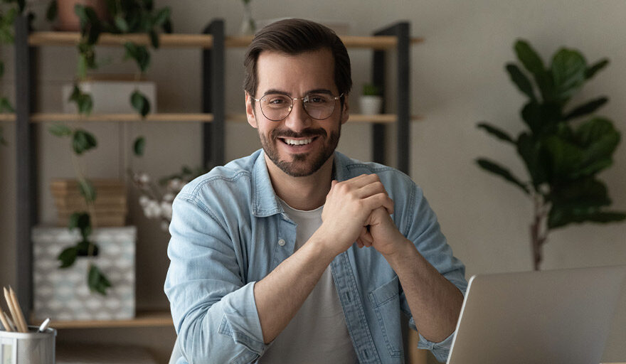 Man with beard and glasses sitting at a desk smiling