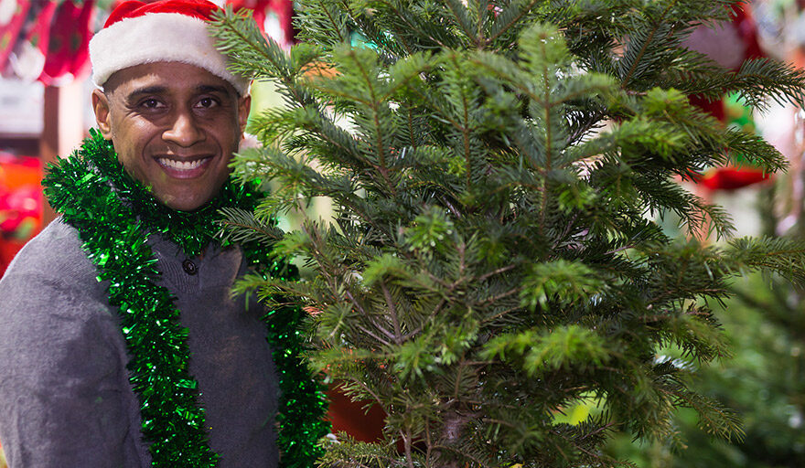 Smiling man in Santa Hat next to a tree in a store.