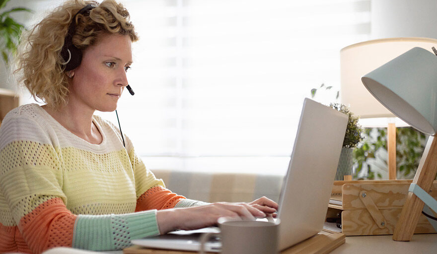 Blonde woman wearing a headset, using a laptop computer and concentrating.