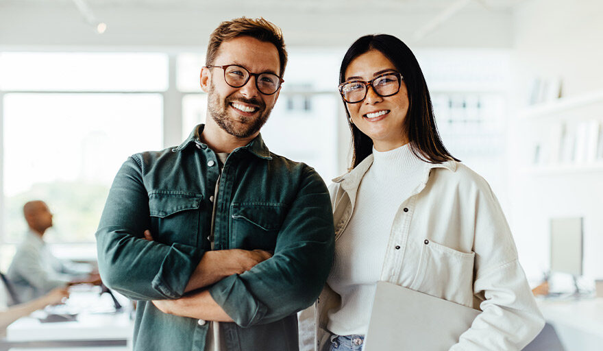 Man and woman in an office environment standing next to eachother and smiling