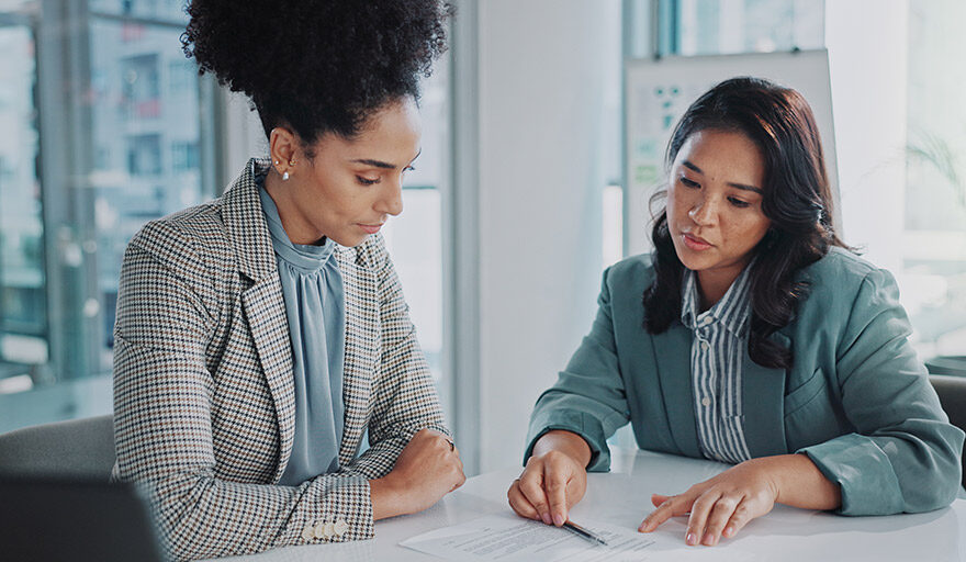 Two professionally dressed women reviewing a document in an office.