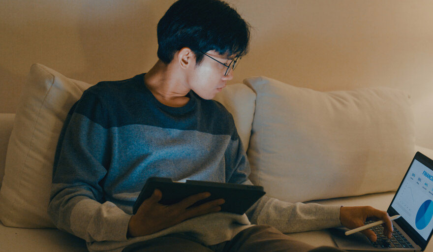 Young man sitting on a couch with a tablet and a laptop.