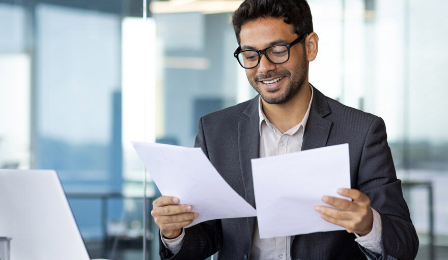 Smiling man, dressed professionally, looking at two pieces of paper