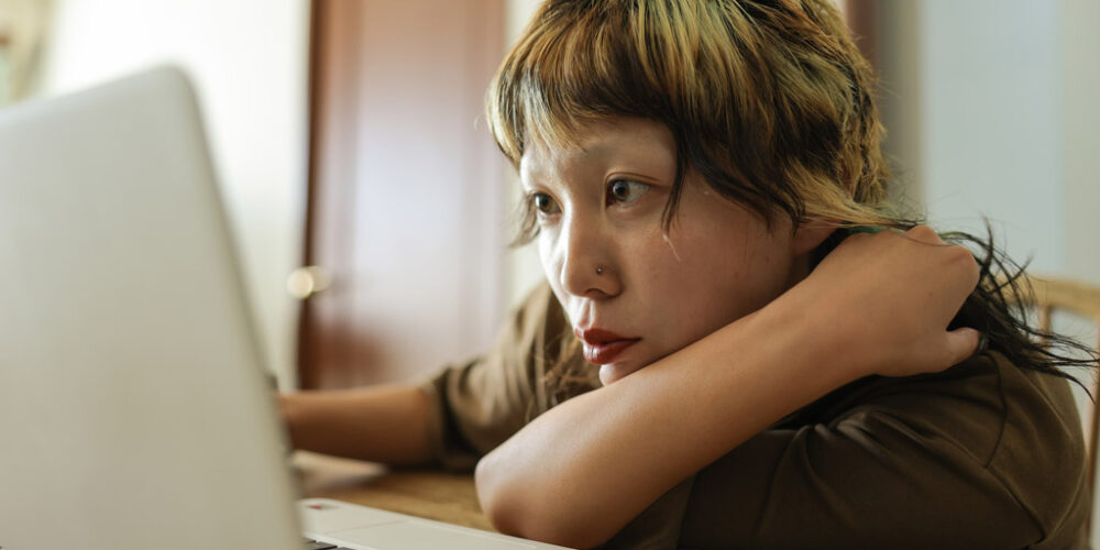 Woman leaning on a desk focused on a laptop computer screen. 