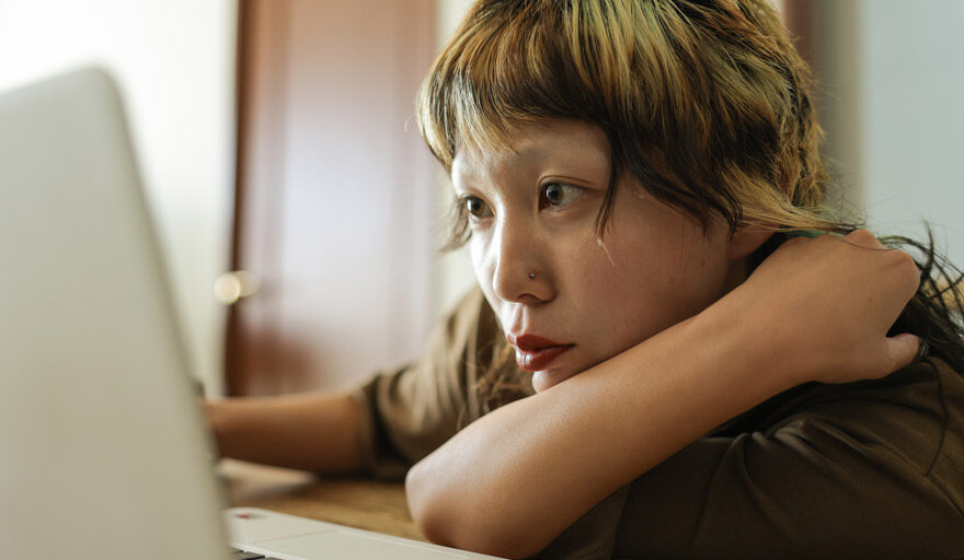 Woman sitting at a desk, leaning forward, looking at a computer screen.