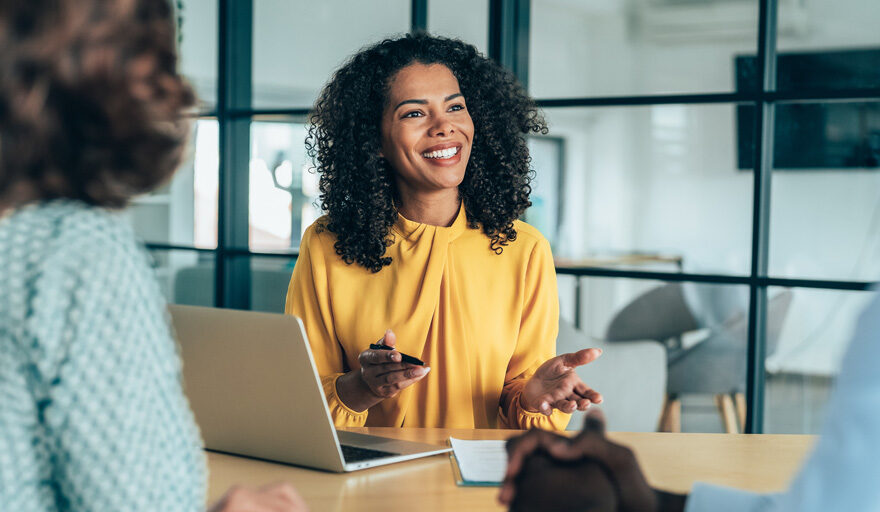 Happy woman in an office setting sitting at a table speaking to colleagues